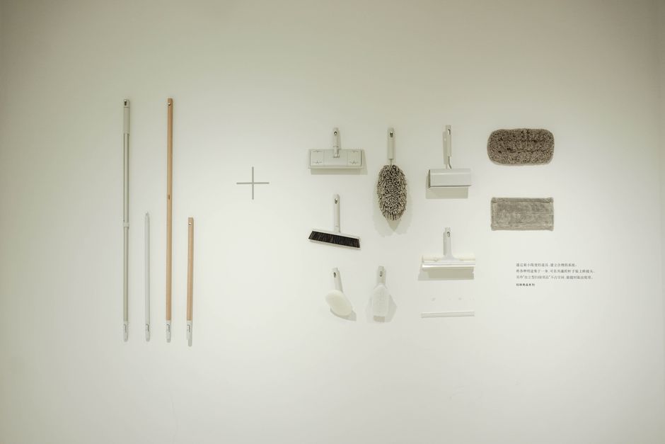 A minimalist flat lay of various cleaning tools arranged on a white wall, showcasing a modern concept.