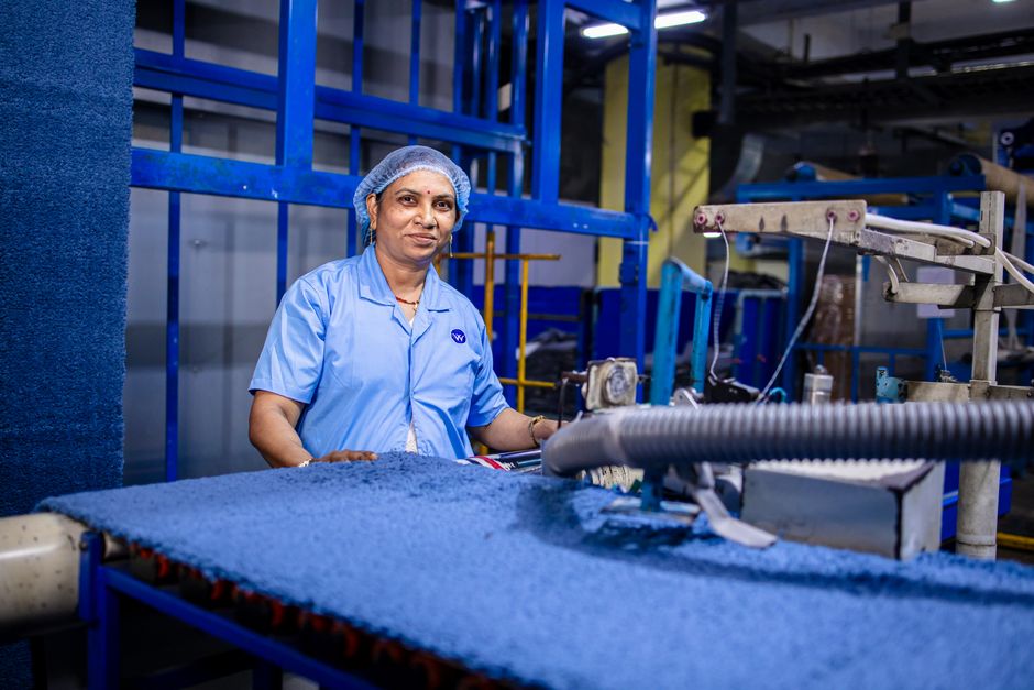 A female factory worker posing near textile machinery in a blue-collar work environment.