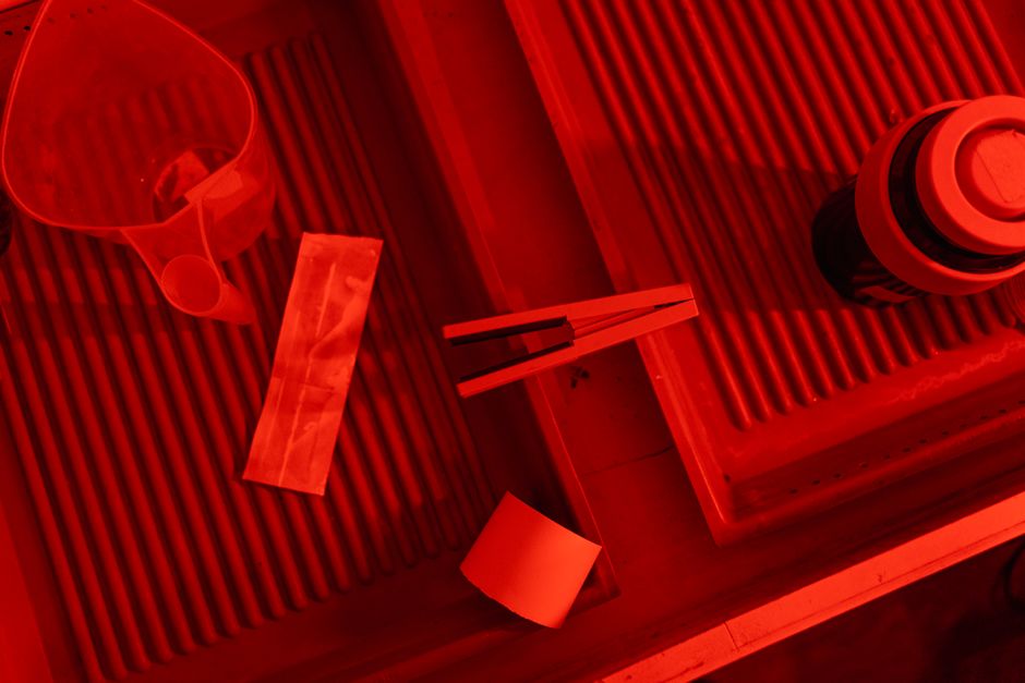 Close-up view of darkroom tools and trays under red lighting, essential for film development.
